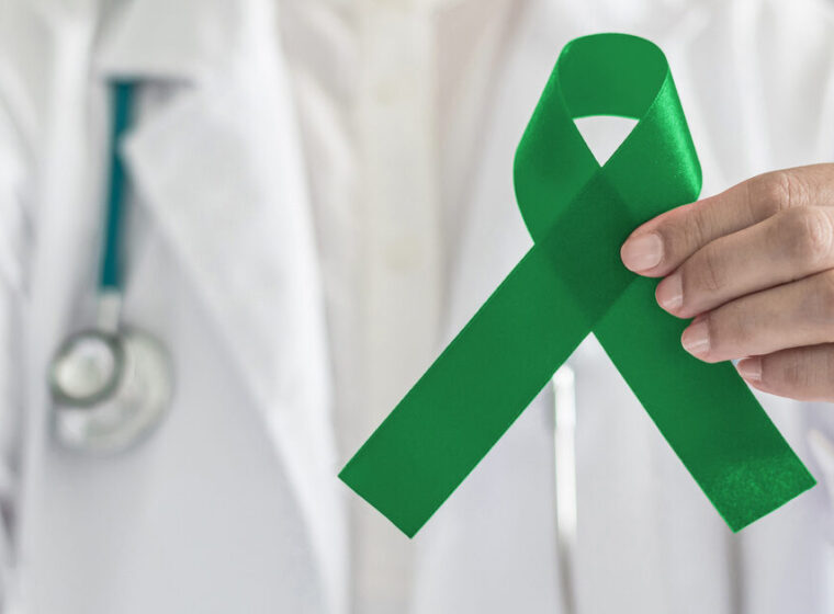 Emerald green or jade color ribbon in doctor’s hand symbolic for Liver Cancer and Hepatitis B disease awareness concept