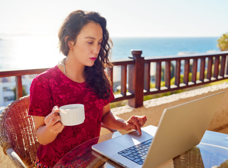 Hispanic woman working on laptop on the building terrace with the Pacific Ocean in the background